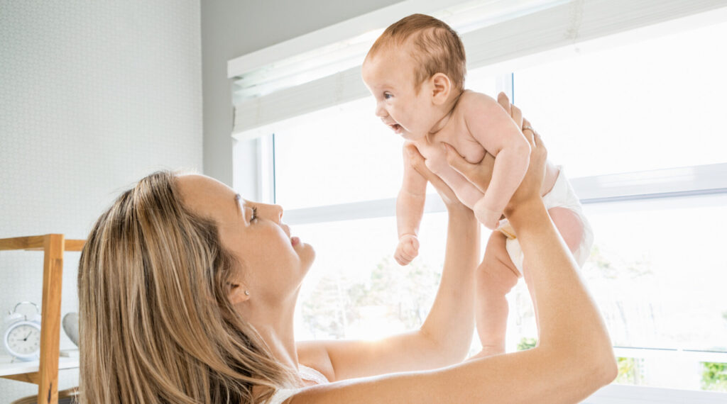 Mutter hällt ihr Baby vor sich auf dem Arm und lächelt es an